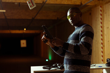 Portrait of person wearing safety goggles loading pistol bullets in chamber, during firearm...