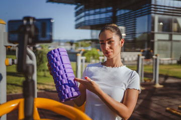 sportswoman at outdoor gym filming herself with foam roller on camera