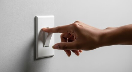 A hand flips a white light switch on a gray wall.