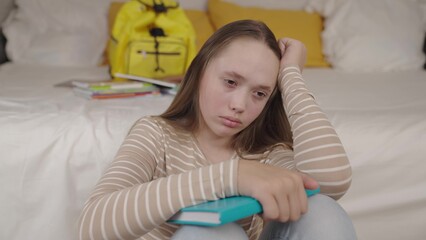 an upset girl with book her hands sits in children's bedroom room, teenager schoolgirl is sad alone...