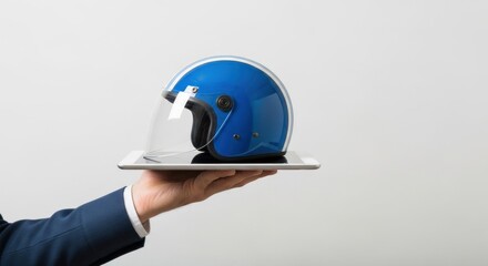 A hand in a suit holds a tablet with a blue motorcycle helmet on it.