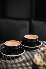 Two black coffee cups on a table in a cozy, modern cafe setting during the afternoon