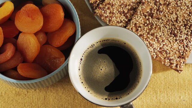 Close-up of a cup of black coffee or instant chicory with dried apricots and crispbread on the table, healthy light snack. High quality 4k footage