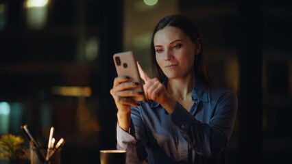 Cheerful woman surfing cellphone internet at night office closeup. Smiling woman