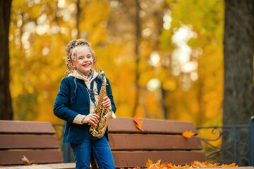Little girl playing saxophone in autumn park on sunny day. Happy child practice music instrument outdoors for music lesson