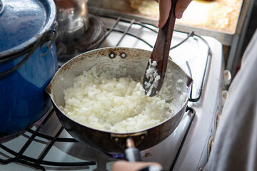 Close-up of a wooden spoon stirring onions in a frying pan