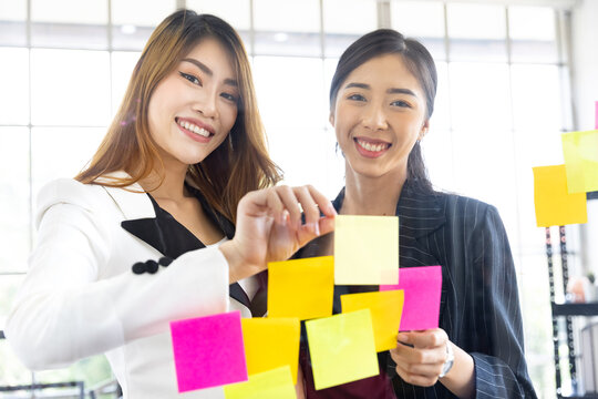 Creative teamwork asian businesswoman putting her ideas on asticky notes on glass wall at office.Business people meeting sharing idea concept. - Powered by Adobe