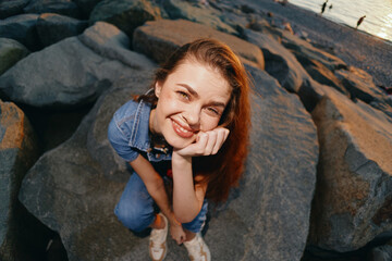 lifestyle woman in modern boho-western denim street style sitting on rocks by water, smiling...
