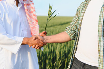 Farmers shaking hands in a wheat field holding a wheat stalk