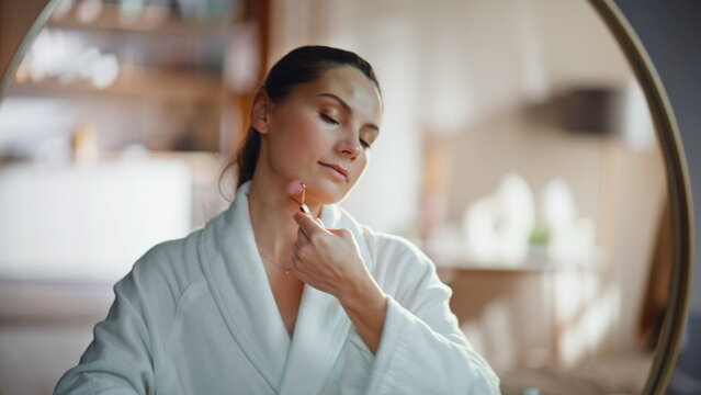 Woman using face roller for self massaging beautiful face in mirror closeup. - Powered by Adobe