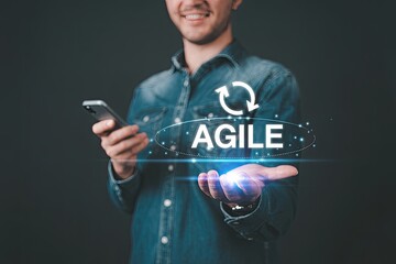 Smiling man holding a smartphone and presenting the word agile with a circular arrow icon above it symbolizing flexibility and adaptability in business processes