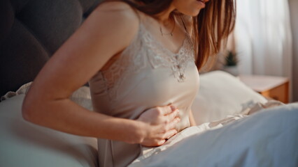 Distressed lady holding stomach in bedroom feeling unwell closeup. Worried woman