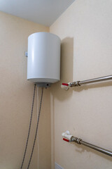 Modern electric water heater installation with visible plumbing connections on a textured wall,...