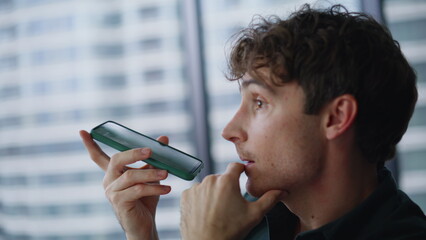 Closeup man recording voice message by cellphone sitting office. Serious manager