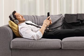 Businessman lying on a sofa and listening to music on headphones at home
