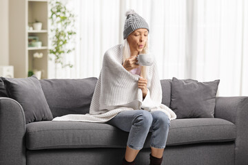 Sick female wrapped in blanket sitting on a sofa
