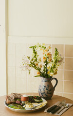 On the table in the cafe there is a plate with breakfast, on which lie several slices of bread, salad, butter, boiled eggs. Next to it on the table is a vase with flowers. Breakfast.  Close-Up.  Soft 