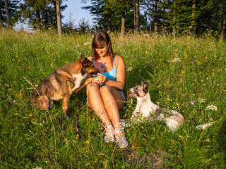PORTRAIT: Cheerful woman sits in a vibrant wildflower field, offering a treat to one of her dogs....