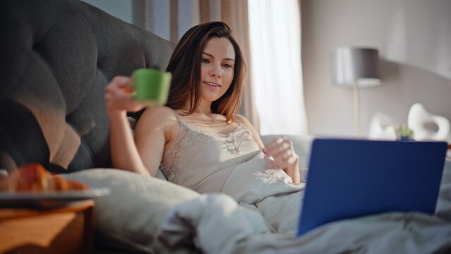 Girl watching movie bed drinking morning coffee closeup. Smiling woman breakfast - Powered by Adobe