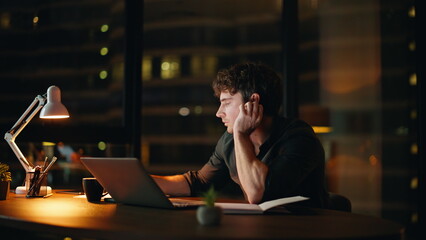 Overtime worker browsing laptop reading papers at night office. Manager tired