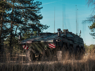 Armored personnel carrier positioned in tall grass field with multiple antennas and communication...