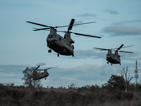 Multiple Chinook helicopters flying in formation over rural terrain with communication tower visible