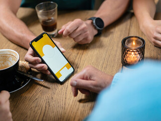 People sitting at wooden table with smartphone, coffee cups, candle and hands visible in casual meeting setting