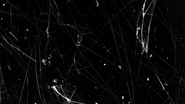 Abstract black background with fine, white, intersecting lines and small light dots, resembling scratches or a complex, delicate web