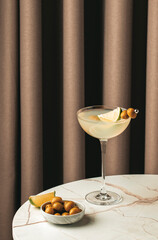 Mexican martini with tequila, lime juice, and green olives on a marble table near soft drapery