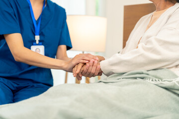 Asian woman caregiver holding senior woman hands and consoling with empathy. Doctor or nurse visit...