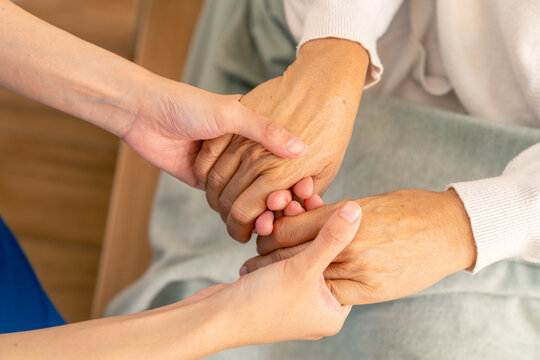 Asian woman caregiver holding senior woman hands and consoling with empathy. Doctor or nurse visit and take care elderly patient at nursing home. Home medical healthcare service and health insurance. - Powered by Adobe