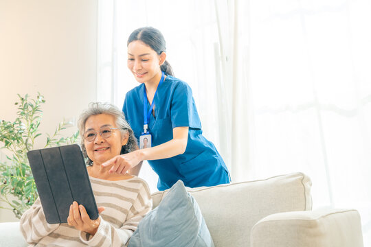Female caregiver take care and teach senior woman using digital tablet with internet for online shopping and health tracking at nursing home. Elderly people home medical wellness healthcare services.