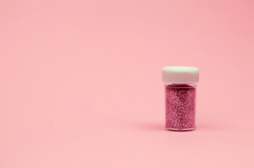 A glass jar brimming with fine pink shimmer is placed on a soft pink surface, glowing with light in...