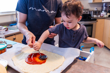 Mother and Toddler Cooking Together Spreading Sauce on Pizza Dough