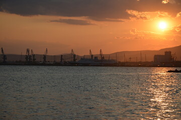 Orange sky and sunset against the backdrop of mountains and a seaport