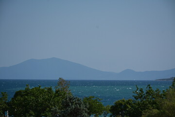 Seascape - blue sea, trees and mountains in the distance