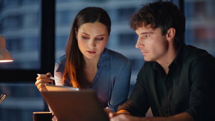 Two managers analyzing project looking tablet data at dark office closeup. 