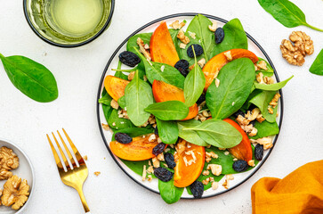 Autumn vegan salad with fresh persimmon, walnuts, raisin and spinach, white background, top view