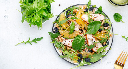Fresh salad with chicken, orange, raisins, mixed herbs and crunchy seeds, white table background, top view