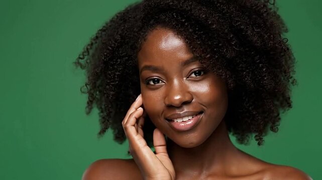 A smiling woman with dark skin curly hair and a hand touching her cheek against a green background