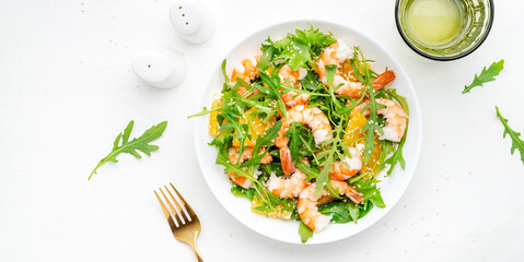 Seafood salad with juicy shrimps and orange, arugula and sesame on white background, top view