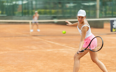 Young woman playing tennis against female opponent on tennis court