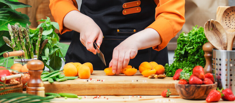 Chef prepares fresh apricots and vegetables on a wooden cutting board in a colorful kitchen filled with greenery. - Powered by Adobe