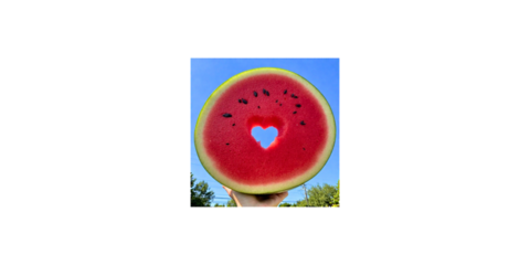 A vibrant slice of watermelon held up against a clear blue sky, featuring a heart-shaped cutout in the center.
