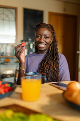 Happy young woman eating strawberries and drinking orange juice for breakfast at home, enjoying a...