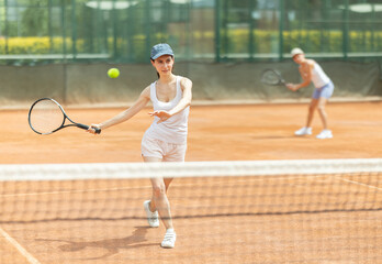 Young woman playing tennis against female opponent on tennis court