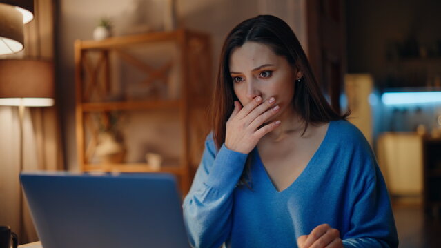 Concerned brunette reading email at laptop in dark home closeup. Desperate woman