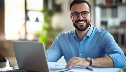 Fototapeta premium Businessman In Modern Office Working On Laptop And Analyzing Data, Holding Documents And Pen, Wearing Glasses, Beard, And Blue Shirt.