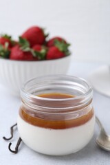 Tasty panna cotta with caramel, vanilla pods and strawberries on light table, closeup