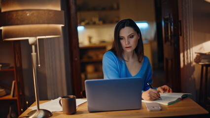 Confident lady creating project looking laptop writing notes night home closeup.